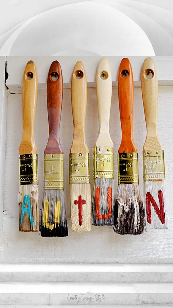Paintbrushes hanging from nails in wood