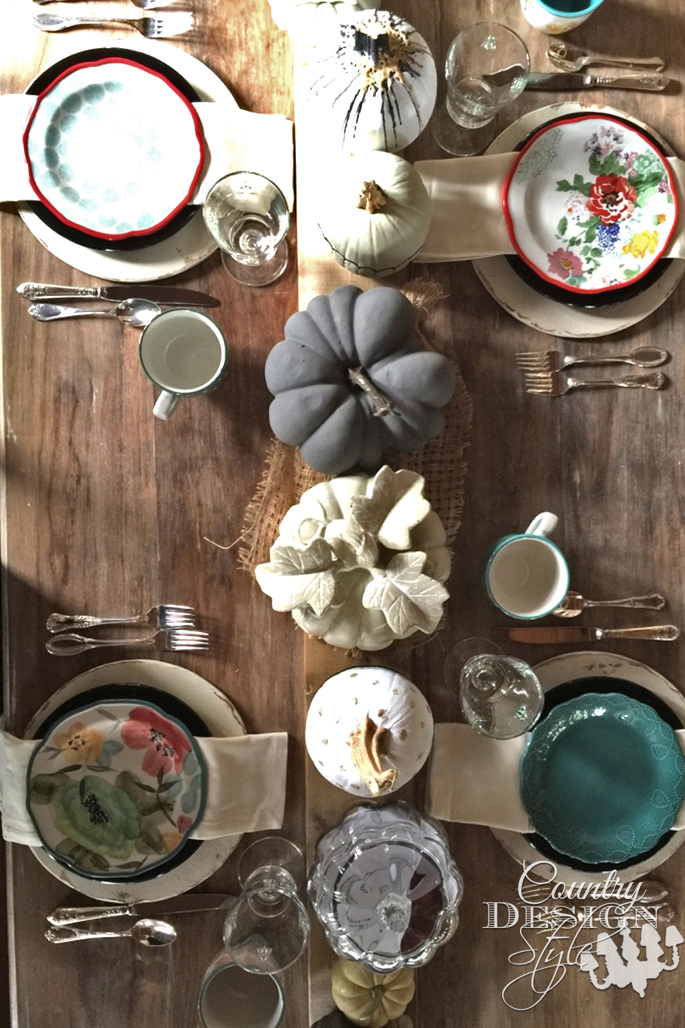 Thanksgiving table with natural colors on different type of pumpkins lined on a wood board runner. The place setting have loads of color with rustic chargers. | countrydesignstyle.com