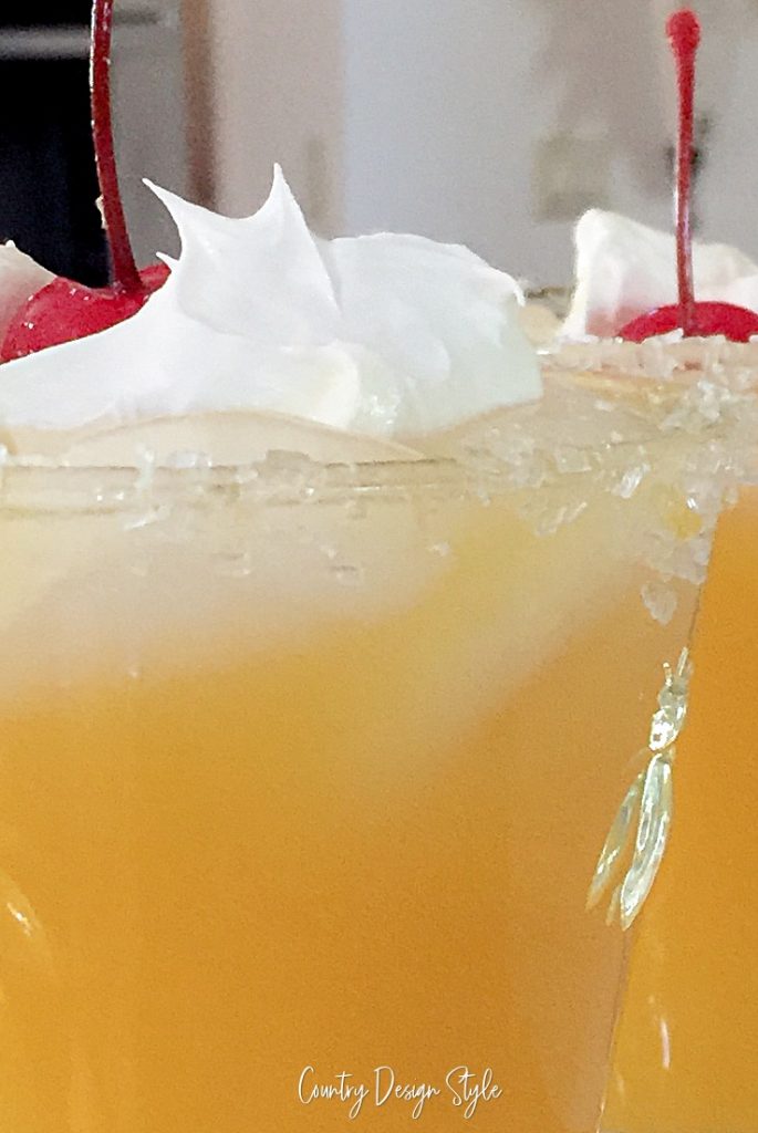 close up of orange juice with cherry vodka topped with whipped cream and cherries. 