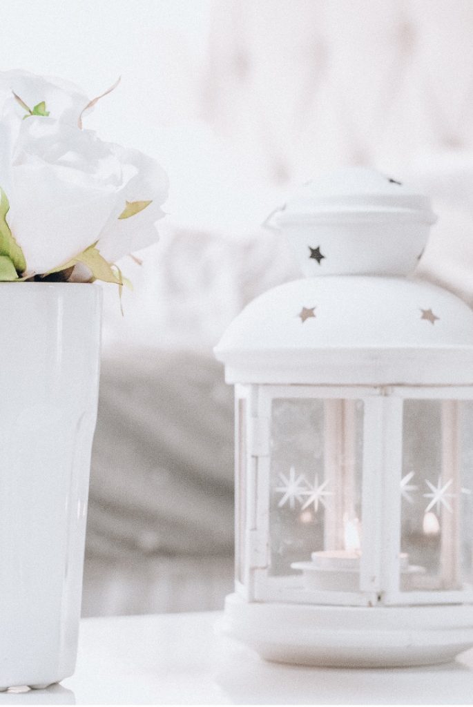 White lantern with small candle and white vase with white flowers.