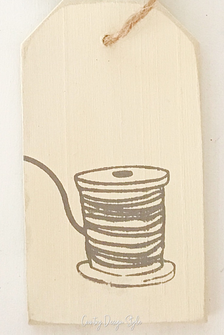 cream painted tag with image of thread spool